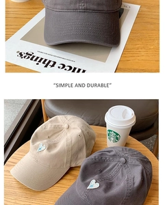 Detail of blue heart embroidery on soft cotton baseball caps in gray and beige colors