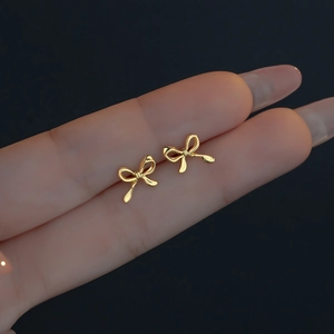 Minimalist golden bow stud earrings shown on fingertip to highlight delicate micro size