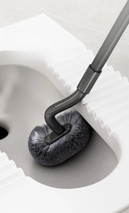 Detail of S-shaped long handle toilet brush cleaning the rim of a ceramic squatter