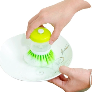 Manual soap dispensing dish brush for kitchen cleaning on white plate with foam