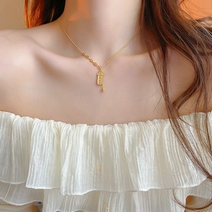 Dettaglio di una collana con ciondolo a cilindro dorato indossata da una modella su camicia