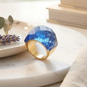 Detail of blue faceted crystal ring on gold band displayed on white marble tray