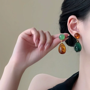 Detail of model wearing resin teardrop earrings in green and amber contrast
