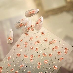 Detail of floral nail stickers with orange petals and golden relief on pearl nails