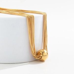 Detailed view of layered gold necklace with geometric ball pendant on a white stand