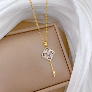 Macro shot of gold clover key pendant with sparkling pavé crystals on a gift box