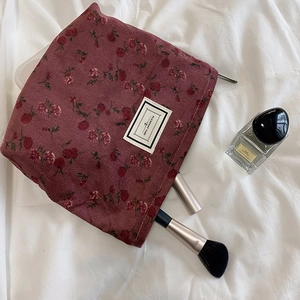 Macro view of burgundy corduroy makeup bag with floral patterns and zipper detail