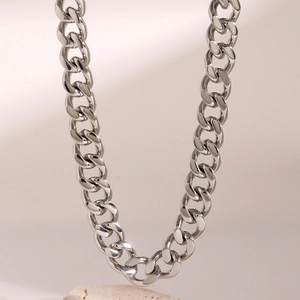 Detailed shot of silver Cuban link chain necklace resting on a textured beige stone base