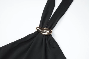 Detail view of a golden buckle on a black backless top showing fabric texture