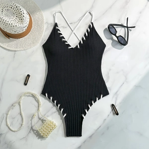 Flat lay of ribbed black one-piece swimsuit with white lace-up detail on marble background