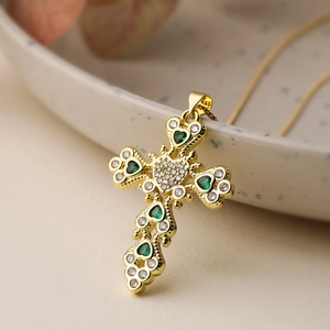 Gold plated cross necklace with green and clear zircon hearts on ceramic background