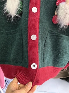 Close-up of green knit cardigan with red ribbed trim, white buttons, and soft wool texture