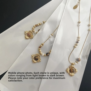 Detail of three gold floral necklaces with tiger eye stones and white beads on black background