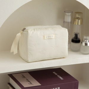 Detail of cream quilted makeup bag with bow embroidery and silk ribbon zipper pull