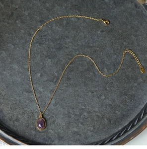 Close-up of a purple teardrop gemstone pendant on a 18K gold-plated titanium steel chain
