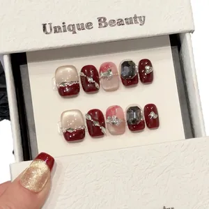 Elegant berry red and gold press-on nails with bow and rhinestone accents