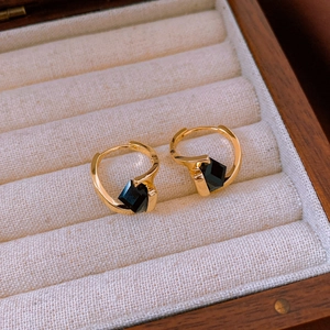 Detail view of gold-plated cubic hoop earrings with black stones in a jewelry box