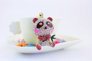 Macro shot of cute rhinestone panda keychain with gold ring on white ceramic background