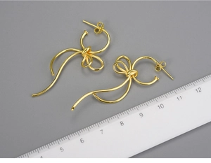 Detail of S925 gold-plated bow drop earrings showing length against a scale ruler
