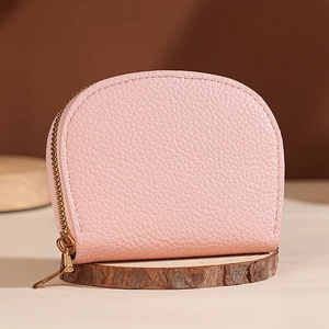 Pink shell shaped leather card holder with pebble texture and gold zipper on wood