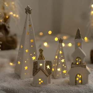 Glowing white and gold ceramic Christmas tree and house ornaments with LED lights and snow