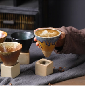 Close-up of conical ceramic coffee mug with dripping blue glaze and cube base