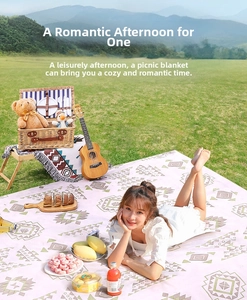 Outdoor picnic mat with pink bohemian geometric patterns shown in a lush green grass setting