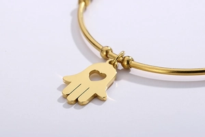 Detailed close-up of a golden Hamsa hand charm with a hollow heart on a sleek metal bangle
