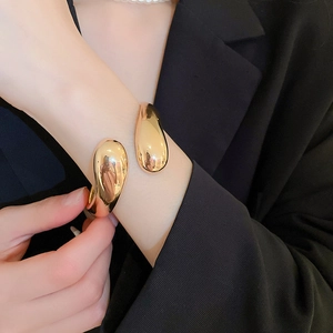 Dettaglio di un bracciale a goccia dorato indossato sopra la manica di un blazer nero
