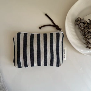 Detail of striped canvas pouch with white zipper and simple wish woven label