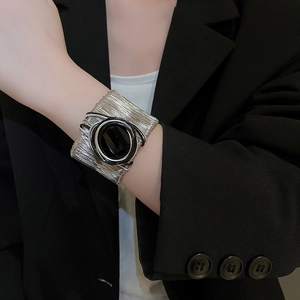 Close-up of a wide silver metal cuff bracelet featuring a central black circular detail