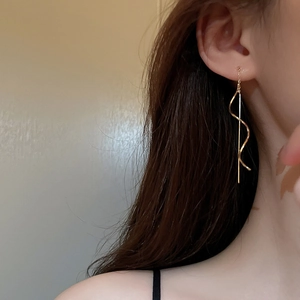 Detailed close-up of golden long tassel chain earrings with spiral and rod design on a model