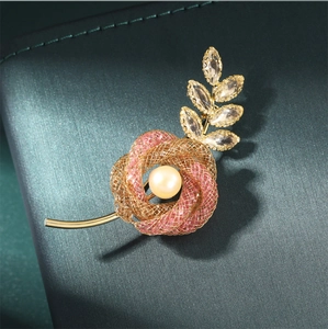 Macro detail of elegant pink flower brooch with golden leaves and pearl accent