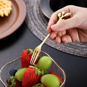 Golden stainless steel leaf-shaped fruit fork picking a strawberry from a bowl