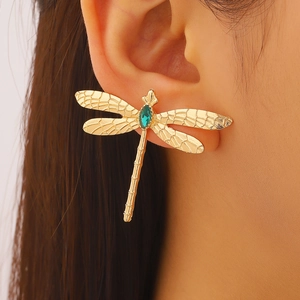 Détail macro de la boucle d'oreille libellule avec gemme verte et ailes ciselées sur modèle