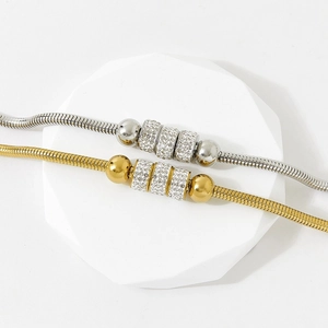 Luxe rhinestone-studded gold and silver snake bone bracelets on a minimalist white stone display