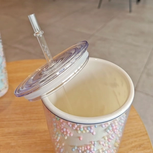 Close-up of double-walled plastic tumbler with colorful beads, transparent lid and straw