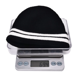 Detail shot of black knit beanie with white stripes on a digital scale weighing 69.4 grams