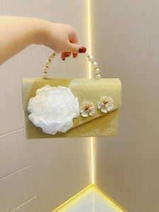 Detail of gold sequin evening clutch featuring large white flower and pearl handle strap