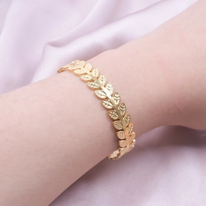 Golden C-shaped laurel leaf stainless steel cuff bracelet worn on a pink silk background