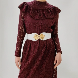 Detail view of a white elastic waist belt featuring two golden metal floral buckles on a model
