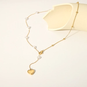 Elegant gold Y-necklace with white heart pearls and a polished heart pendant on a beige stand