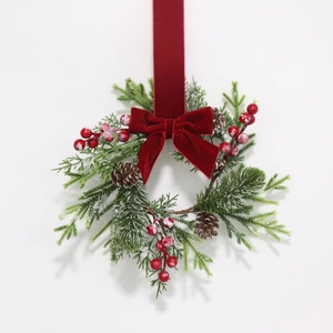 Close-up of Christmas wreath with pine branches, red berries, and velvet ribbon bow