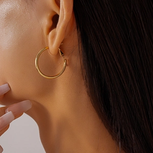 Close-up of large polished gold geometric hoop earrings worn by a model in warm light