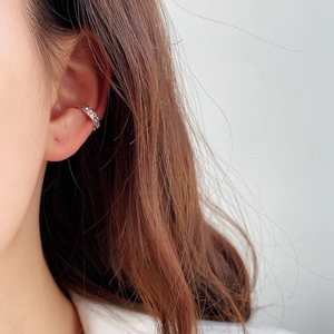 Close-up of a silver ear cuff with woven texture on a model's ear cartilage