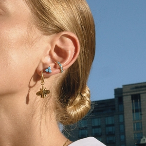 Detail of bee dangle earrings and turquoise ear cuff set worn by a model against blue sky