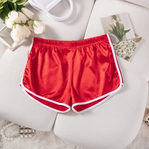 Red satin sports shorts with white piping shown flat on a sofa with fashion accessories