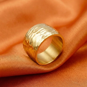Close-up of golden stainless steel ring with hammered texture on orange silk background