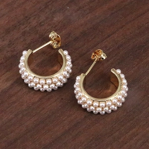 Macro shot of gold hoop earrings with three rows of elegant white pearls on wooden base