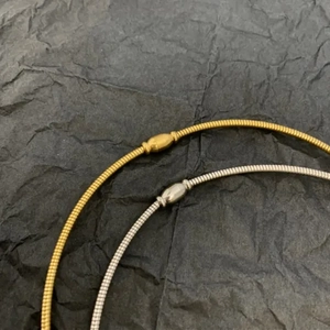 Detail of gold and silver snake chain necklaces with minimalist curved tube pendant